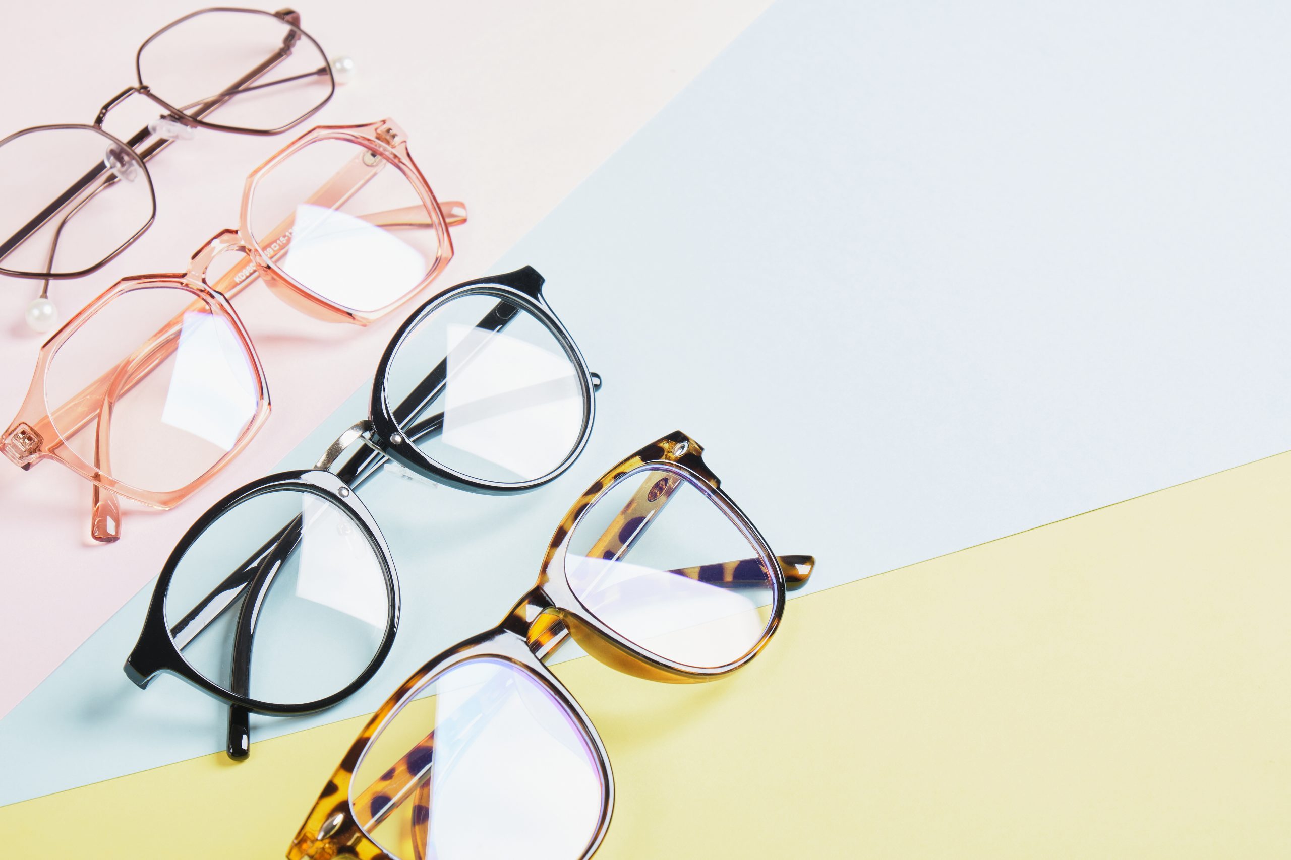 multiple eyeglasses on a multicolored background of pastel colors, geometric background, pink yellow and light blue colors, trendy eyeglass frames